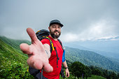 A positive traveler invites you to the mountains, extending his hand into the camera.
