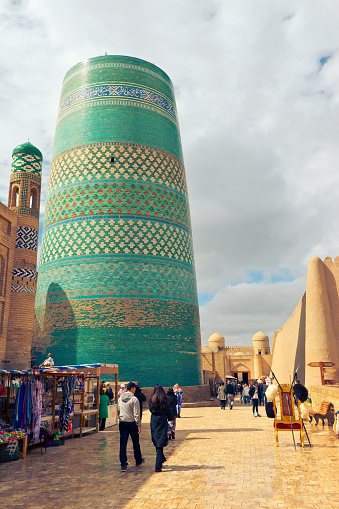 Khiva, Uzbekistan - March 26, 2024: people walk through the streets in the heart of ancient fortress Ichan Kala. View of unfinished building of Kalta Minor minaret