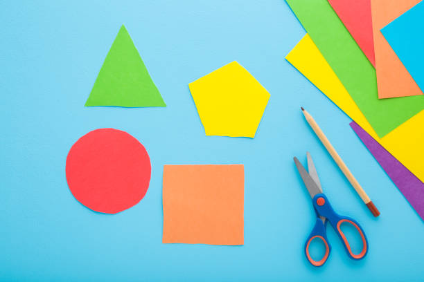 istock Colorful geometric shapes, scissors, pencil and application paper on light blue table background. Pastel color. Closeup. Child made different forms for learning. Top down view. 2149234356