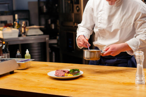 istock chef in the kitchen is about to garnish with sauce a medium rare sliced beef steak on white plate 2149237214