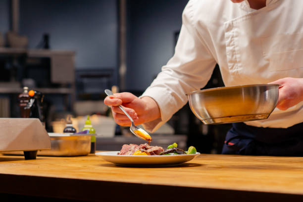 istock close up chef in the kitchen garnishes medium rare sliced beef steak with sauce on white plate with a spoon 2149237443