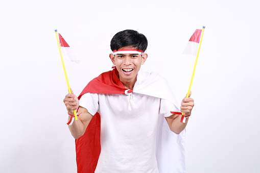 Excited Asian young boy with red white ribbon for celebrating Indonesia independence day standing while holding Indonesia flag