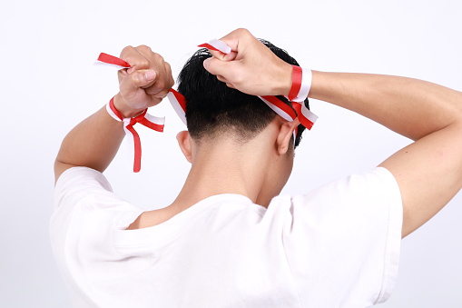 close up photo of Asian man celebrating Indonesian independence tying a red and white ribbon on his head facing backwards