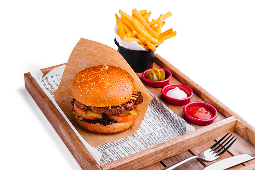 Delicious cheeseburger with golden fries, served on a wooden tray with sauces