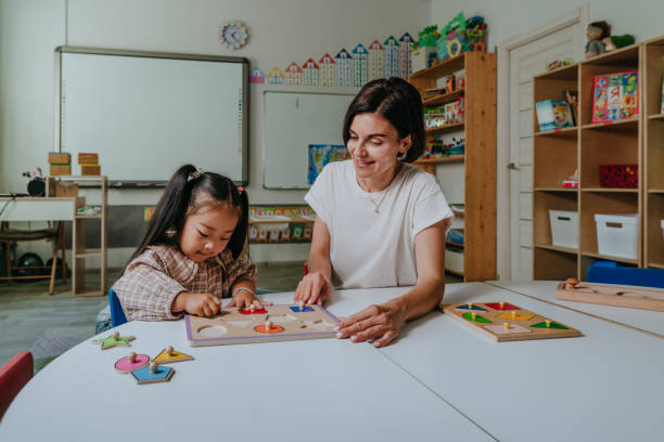 Girl and teacher playing with educational wooden toys in a kindergarten Girl and teacher playing with educational wooden toys and sort geometric shapes in a kindergarten. Selective focus. sorter machine stock pictures, royalty-free photos & images