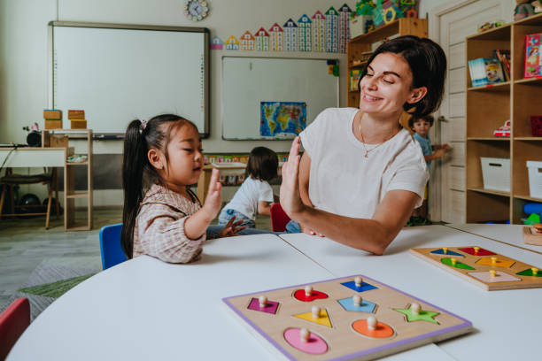 Girl and teacher playing with educational wooden toys in a kindergarten Girl and teacher playing with educational wooden toys and sort geometric shapes in a kindergarten. Selective focus. sorter machine stock pictures, royalty-free photos & images