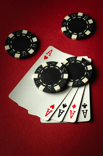 Four aces and black chips on a red table in a casino. Concept of winning with a four of a kind or quads combination in a poker club.