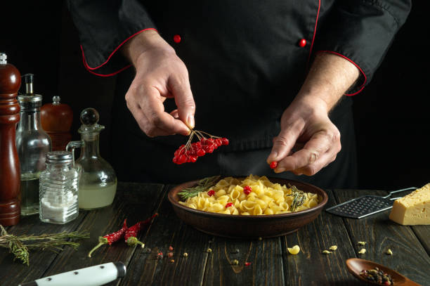 The chef adds viburnum berries to a bowl of pasta on the kitchen table. Low key concept of preparing delicious dinners in a pub