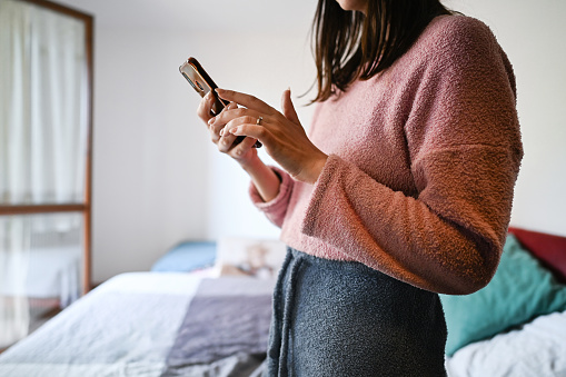 side view portrait of unrecognizable woman using telephone in a bedroom.