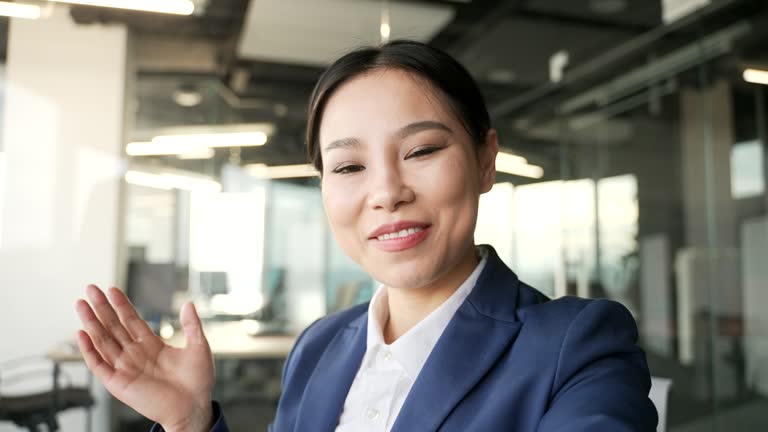 POV Smiling asian businesswoman in formal suit is having video call using phone in business office.