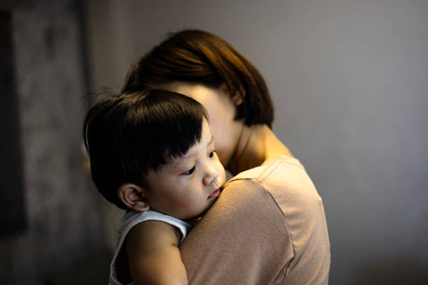 Mother carries the child in her arms. Little boy lies in his mother's shoulder. Sad son hugs mom.
