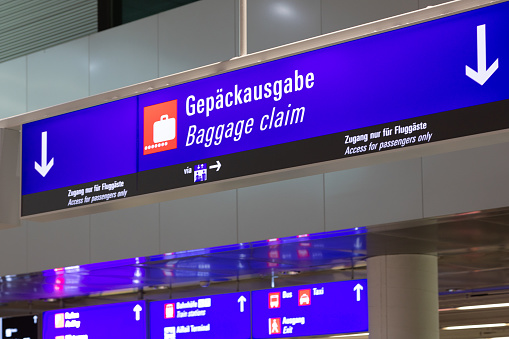 A blue information board in an airport terminal with arrows indicating downstairs to the baggage claim