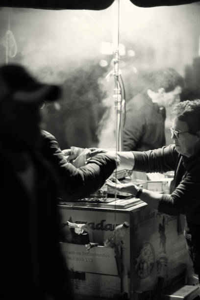 Lisbon, Portugal - December 17, 2022:  A traditional roasted chestnuts vendor attends a client at the Praça do Comércio square in Lisbon downtown.