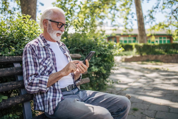 istock Smiling senior man browsing the news on his phone while sitting on a park bench. 2149245012
