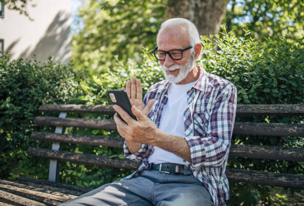 istock Senior man old sitting on a bench outdoors and talking on a video call. 2149245583