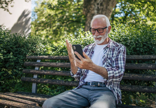 istock Senior Old Man Browsing Internet Smartphone While Sitting Outdoor on a Bench. 2149245616