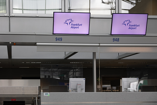 Frankfurt International Airport, Germany - February 19, 2024: displays with advertisement for the Frankfurt Airport hanging above empty check-in counters