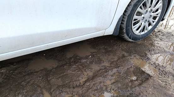 White car on dirty road. Auto stuck in mud, Wheel is submerged. Concept of off-road driving. Puddles. Washing the body. Cleaning vehicle. Corrosion protection concept. Abandoned automobile. unsafe
