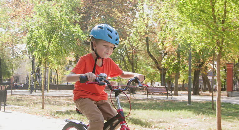 Boy in helmet engages in riding bicycle along alley in park