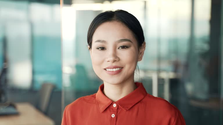 Close up portrait of a young confident asian female employee standing at the workplace in a business office.