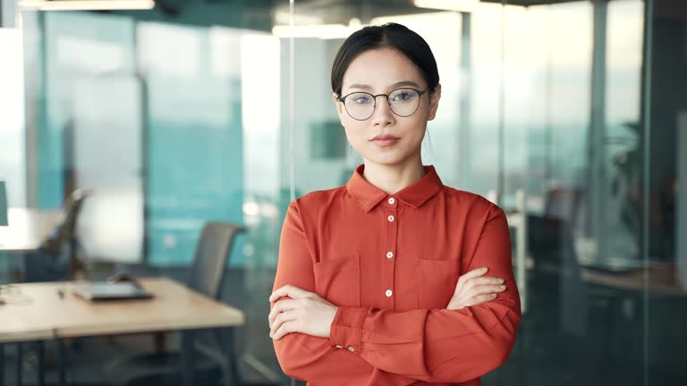 Portrait of a young confident asian female employee standing with crossed arms in a business office
