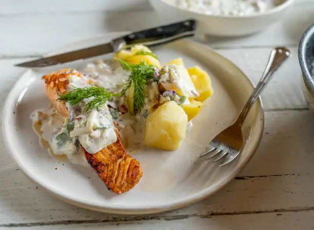 Pan fried salmon fillet with light yogurt apple dill sauce and boiled potatoes on a plate on kitchen table