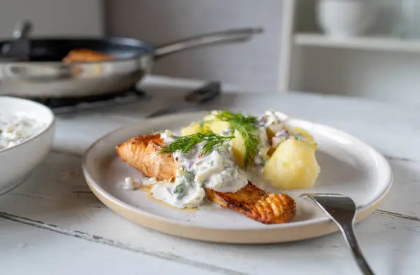 Pan fried salmon fillet with light yogurt apple dill sauce and boiled potatoes on a plate on kitchen table
