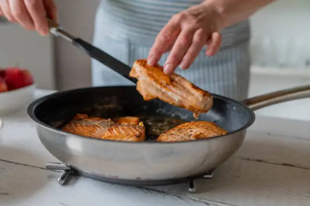 Woman serving fresh seared salmon fillet out of a pan in the kitchen