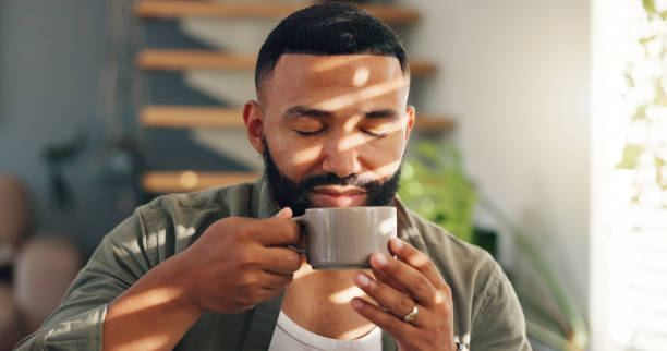 istock Smile, calm and man with coffee by window in apartment for relaxing weekend morning routine. Happy, peace and young male person drinking cappuccino, tea or latte in cup with aroma at modern home. 2149251046