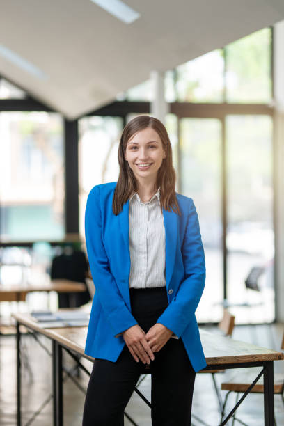 istock A professional woman with a confident smile stands in a bright, airy office space, dressed in a smart blue blazer with arms crossed. 2149251431