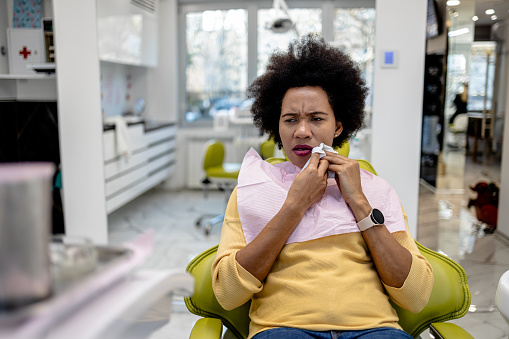 In a small office, a patient sits anxiously in the dentist's chair, touching their painful tooth, waiting for a professional diagnosis and relief from dental discomfort