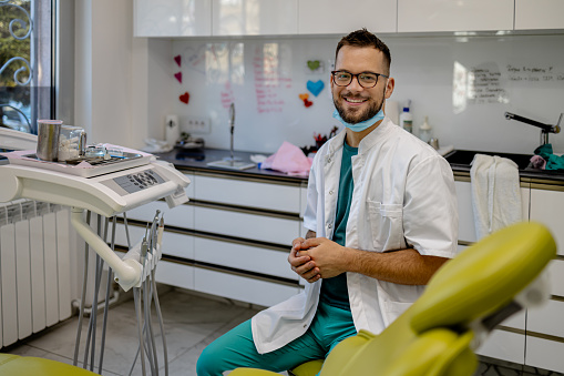 A dentist in a small office smiles warmly at his patient, building trust and demonstrating expertise in dental health and hygiene