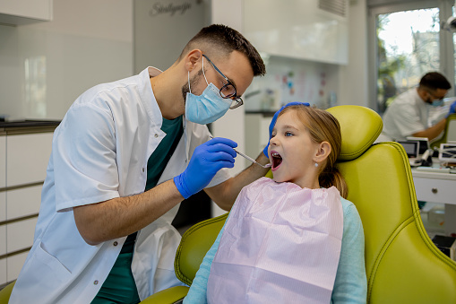 A young patient, smiling broadly, is shown how to brush properly by a dentist in a clinic, focusing on teaching good dental hygiene practices
