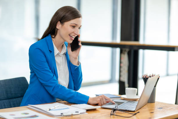 istock Young professional woman engaged in a phone conversation while working on her laptop at an organized office desk. 2149253029