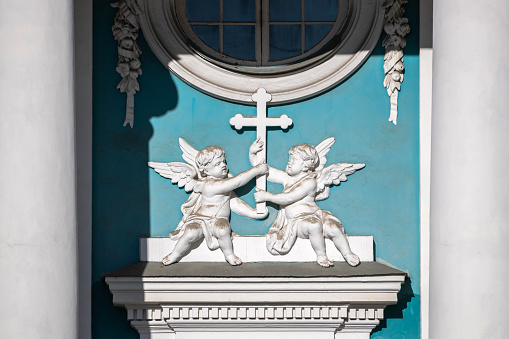 Two angels holding a cross against the background of a church window: religious sculptural element.