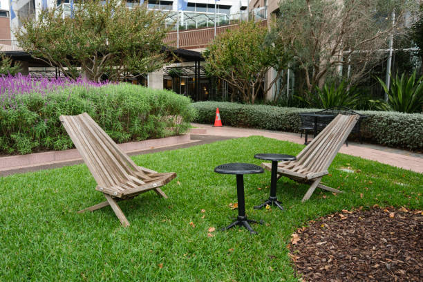 Two wooden chairs on grass with two small tables in a small park.