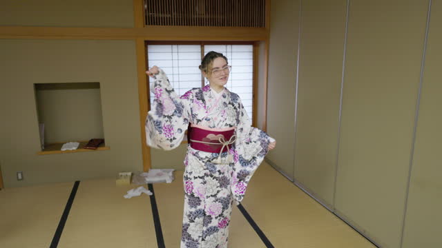 Young female tourist in kimono learning Japanese dance in Japanese tatami room