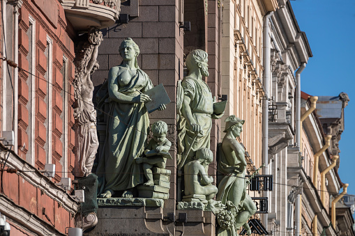 Sculptural group on a building facade: woman with a book, man with tools, children with books. Background - urban architecture.