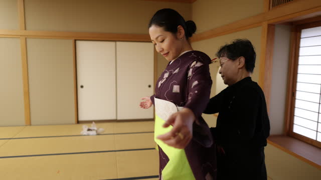 Female tourists getting kimono dressed in Japanese tatami room, wearing green obi sash - part 2 of 2