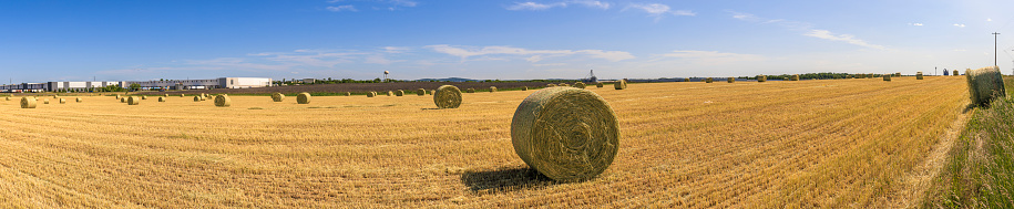 Straw bales on harvested field in front of the barns and country houses on a hill on Pennsylvania farmland. Stitched image