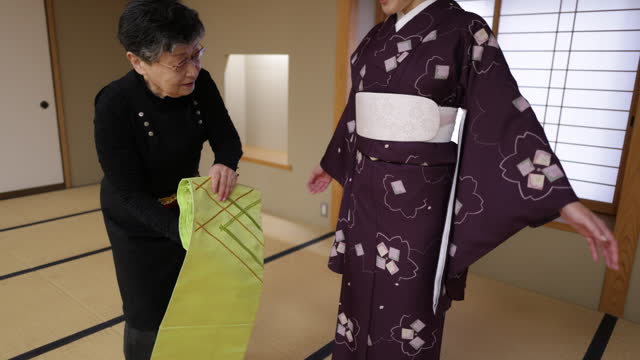 Female tourists getting kimono dressed in Japanese tatami room, wearing green obi sash - part 1 of 2