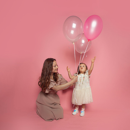 Pretty young woman and baby girl daughter with ballon on pink background