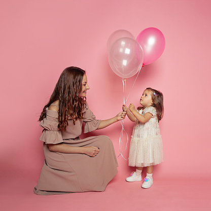 Portrait of pretty young woman and baby girl daughter holding ballon on pink background