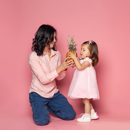 Pretty brunette woman and baby girl with fruit on pink background