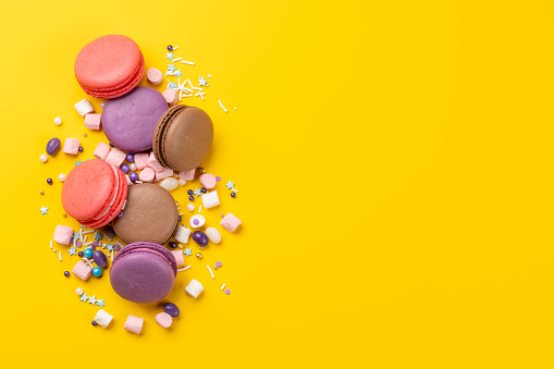 Various colorful macaroons. Flat lay over yellow background with copy space