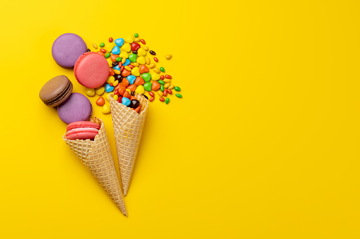 Various colorful candies, lollipops, and macaroons. Flat lay sweets over yellow background with copy space