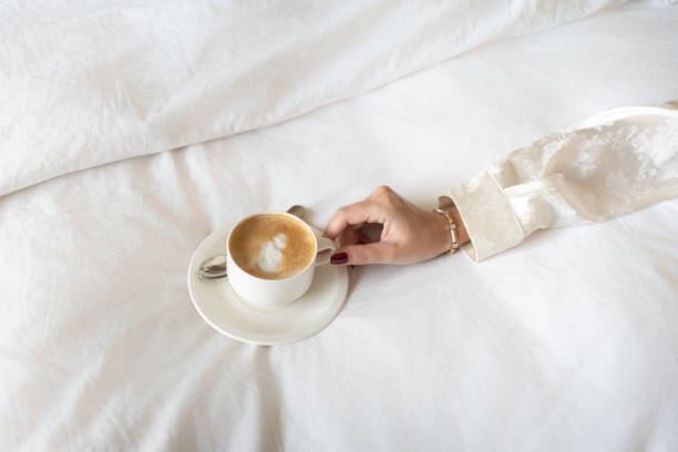 istock A woman's hand holding a cappuccino on white bed linens 2149256870
