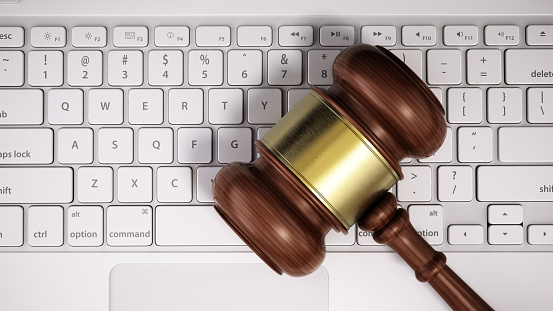 A wooden judges gavel lying on the keys of a white computer keyboard, symbolizing the interaction between legal proceedings and digital technology. The image suggests a concept of online justice or internet law services, possibly depicting the modernization of legal practice.