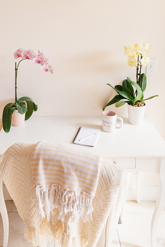 A Mother's Simple Springtime Home Office Space with Pink & Yellow Orchid Plants, a Pad of Paper, a Pen, a Cell Phone & a Mug of Black Coffee with the Word 