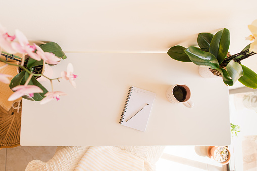A Mother's Simple Springtime Home Office Space with Pink & Yellow Orchid Plants, a Pad of Paper, a Pen, a Cell Phone & a Mug of Black Coffee with the Word 